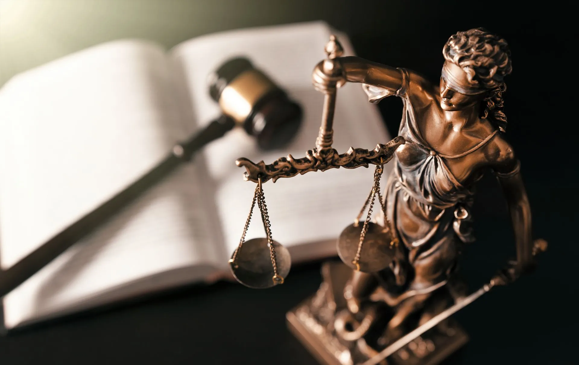 A statue of justice holding a gavel and scales of justice in front of an open book.